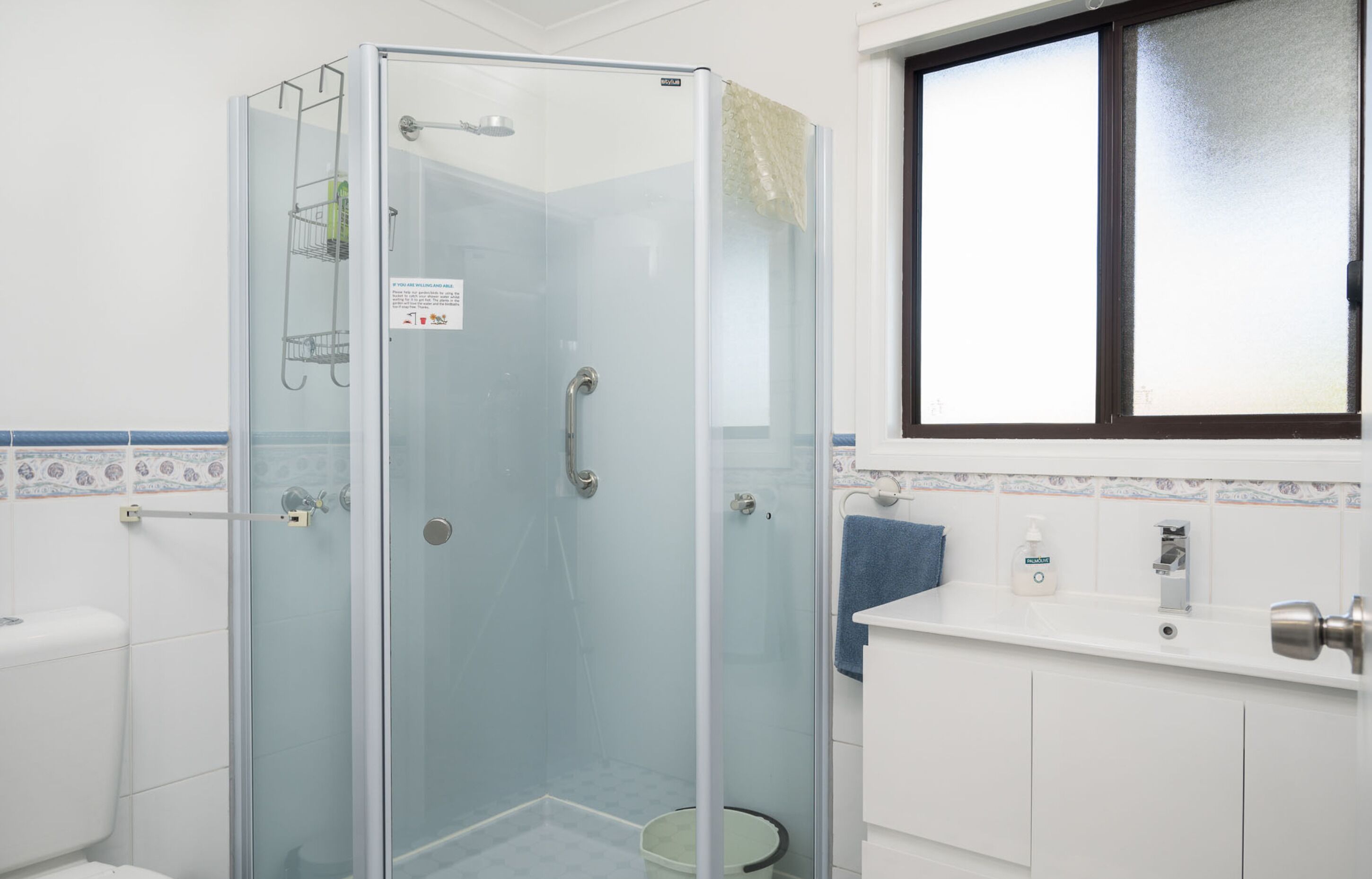 A bathroom with a glass-enclosed shower, a toilet, a sink with a towel, and a window.