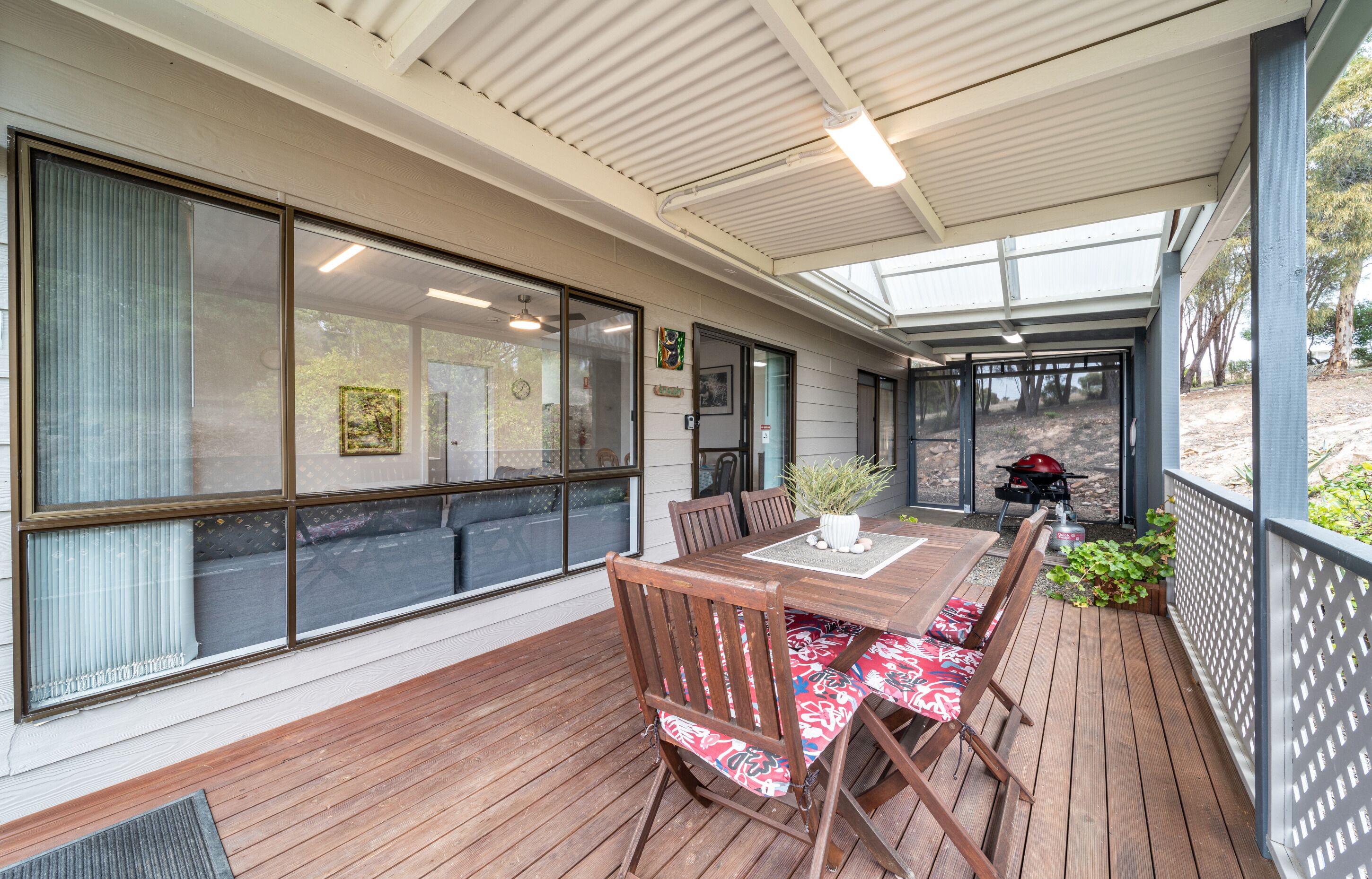 A covered patio with a wooden table and chairs, large windows, and a view of the outdoors.
