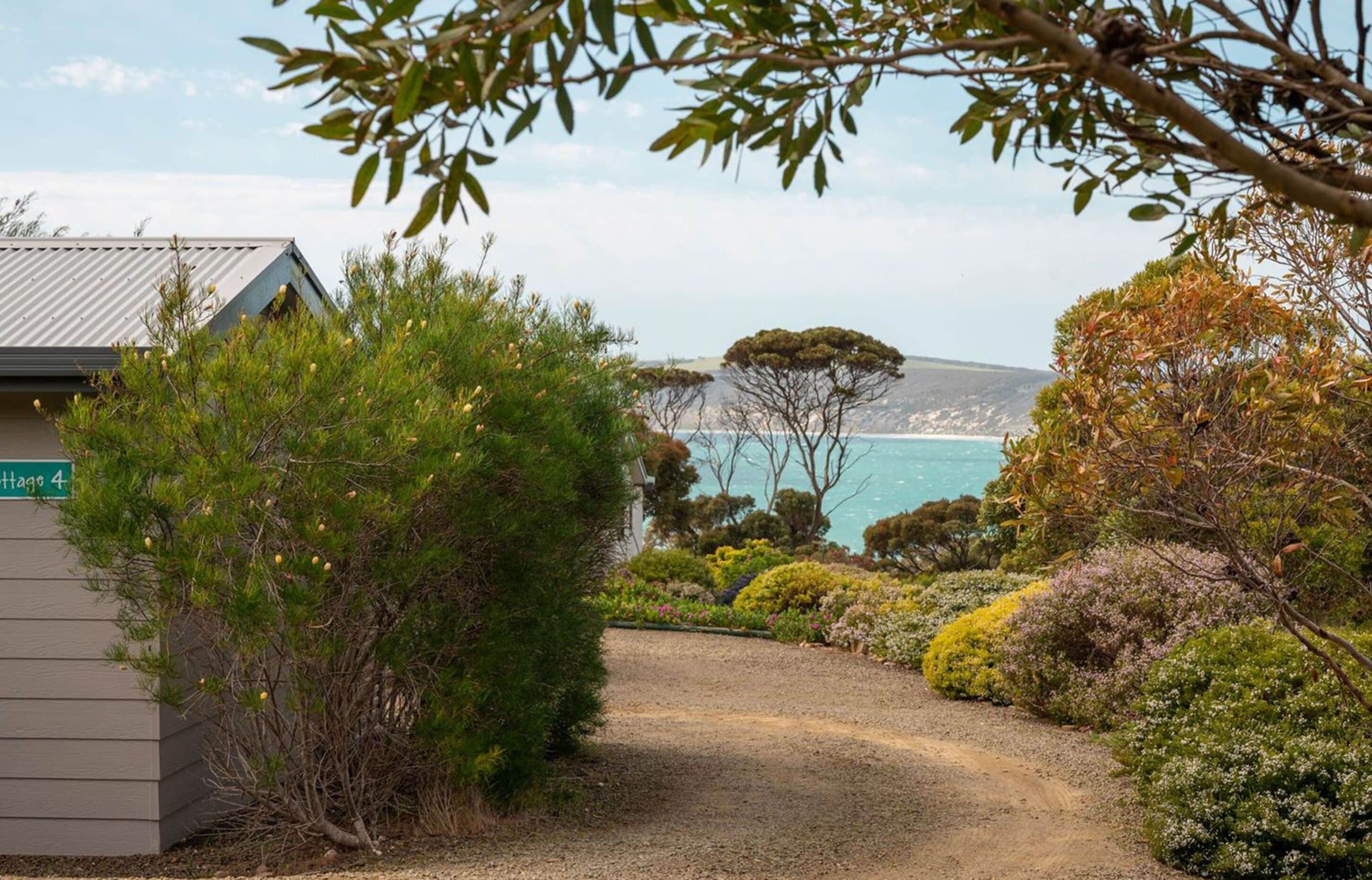 A gravel path leading to a building labeled "Hacienda 4" with a view of the sea and a small island in the distance.
