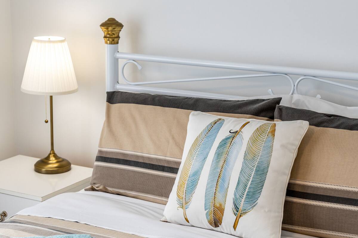 A neatly made bed with striped bedding and a decorative pillow with feather patterns.