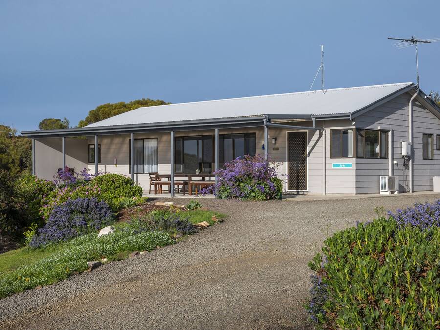 A modern building with a covered patio, a gravel driveway, and surrounding landscaped gardens.