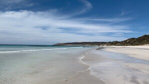 A wide sandy beach with gentle waves, a clear sky, and a distant hilly landscape. - Emu Bay Holiday Homes (Emu Bay)