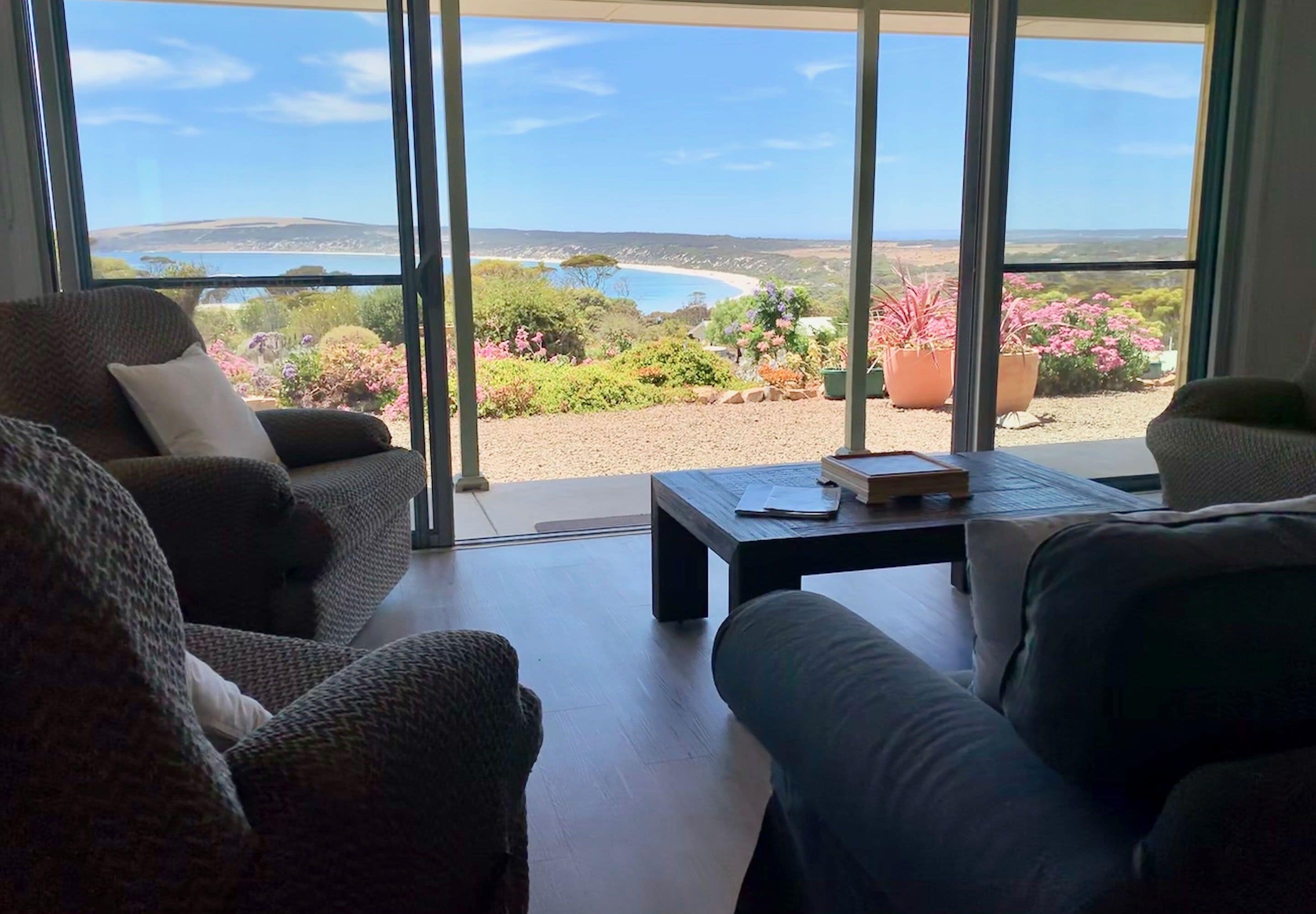 A living room with a view of a coastal landscape, featuring a sofa, a coffee table, and a potted plant.