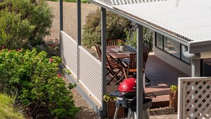 A covered outdoor area with a view of the ocean, a barbecue grill, and a dining table with chairs. - Emu Bay Holiday Homes (Emu Bay)