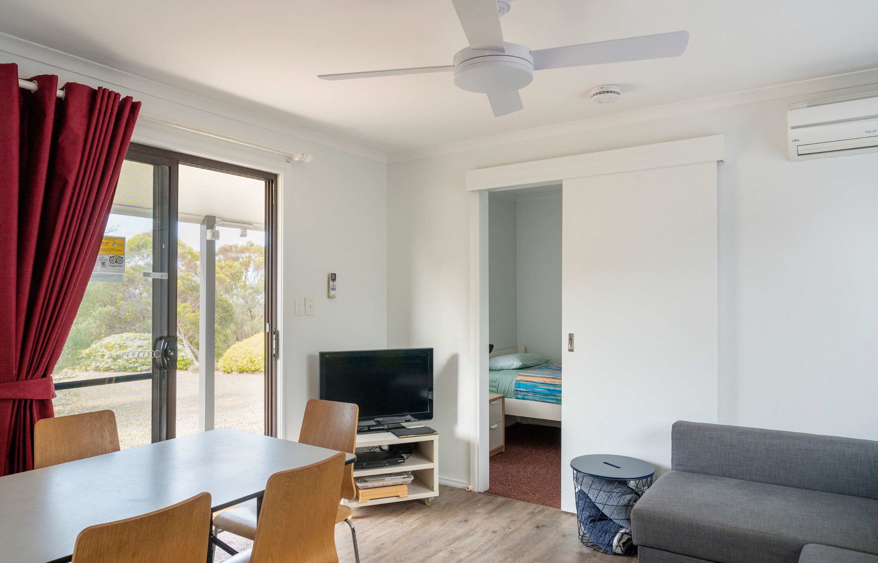 A room with a dining table, chairs, a television, a sofa, and a bed.