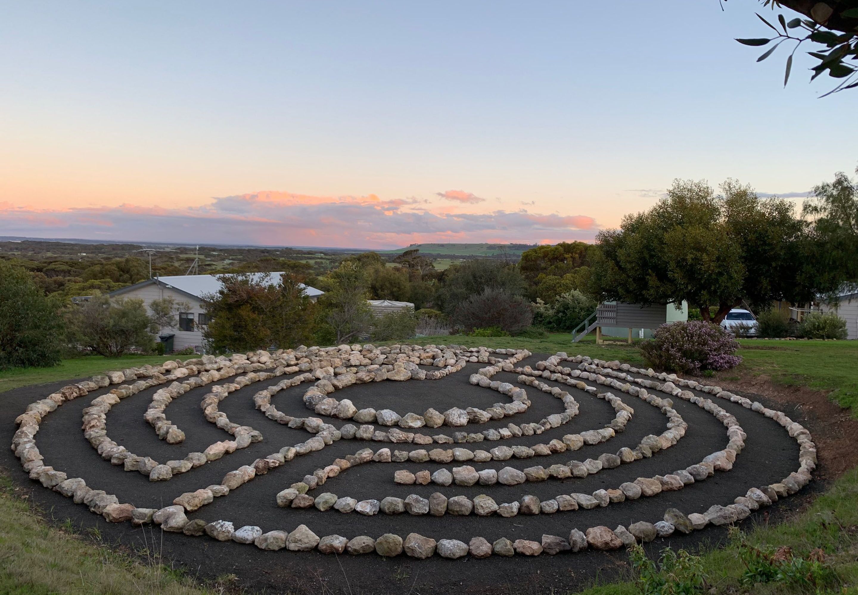 A circular stone labyrinth garden with a clear view of the surrounding landscape and distant hills.