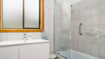 Ein Badezimmer mit einem weißen Waschbecken, einem Spiegel mit Holzrahmen, einer Duschkabine aus Glas und einer weißen Toilette.