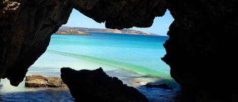 A natural rock formation with a clear view of a turquoise sea and distant land.