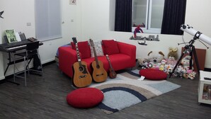 A room with a red sofa, two guitars, a keyboard, a telescope, and various stuffed toys. - Jia Mei Fa Homestay (Taitung)