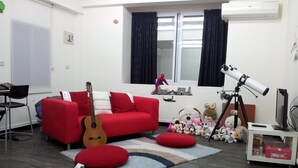 A living room with a red sofa, a guitar, a telescope, and various stuffed toys. - Jia Mei Fa Homestay (Taitung)