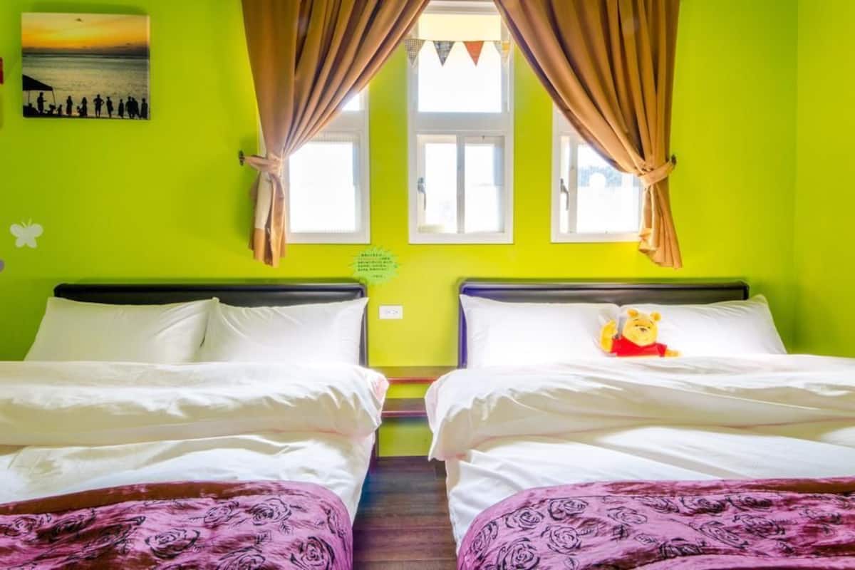 A room with two beds, a window with curtains, a picture on the wall, and a Winnie the Pooh pillow.