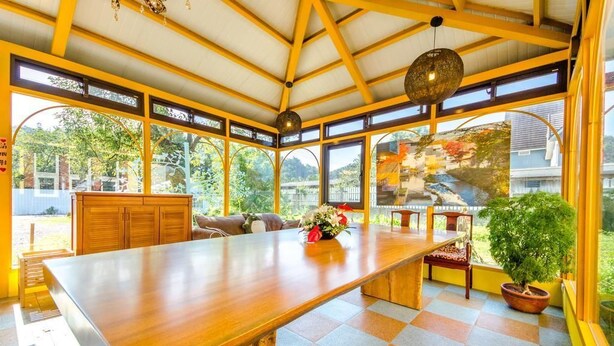 A spacious room with a large wooden table, multiple seating areas, and large windows offering views of the outdoors. - Sunshine House (Dongshan)