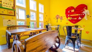 A bright yellow room with a wooden dining table, chairs, and a heart-shaped shelf with toys. - Sunshine House (Dongshan)