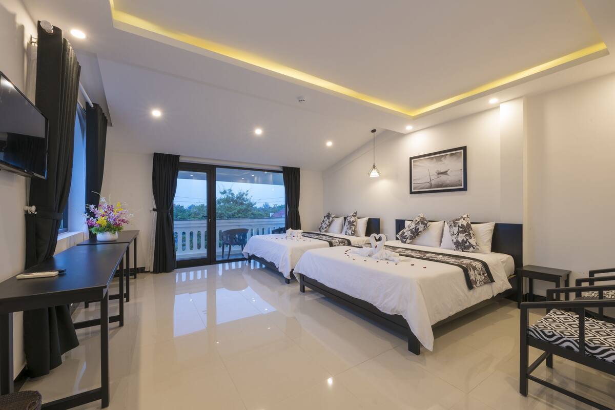 A modern hotel room with two beds, a balcony, a dining area, and a TV.
