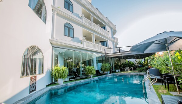 A pool area with a glass-enclosed building, outdoor seating, and a covered patio. - Hoianation Villas Hotel (Da Nang)