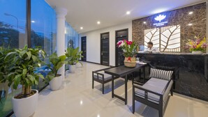 A modern hotel lobby with a reception desk, seating area, and potted plants. - Hoianation Villas Hotel (Da Nang)