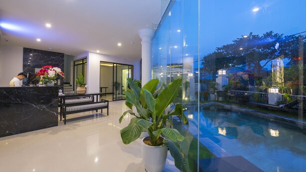 A hotel lobby with a reception desk, seating area, and a pool. - Hoianation Villas Hotel (Da Nang)