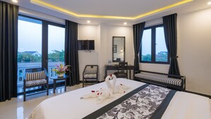 A hotel room with a large bed, a desk, a chair, a TV, and a balcony with a view. - Hoianation Villas Hotel (Da Nang)