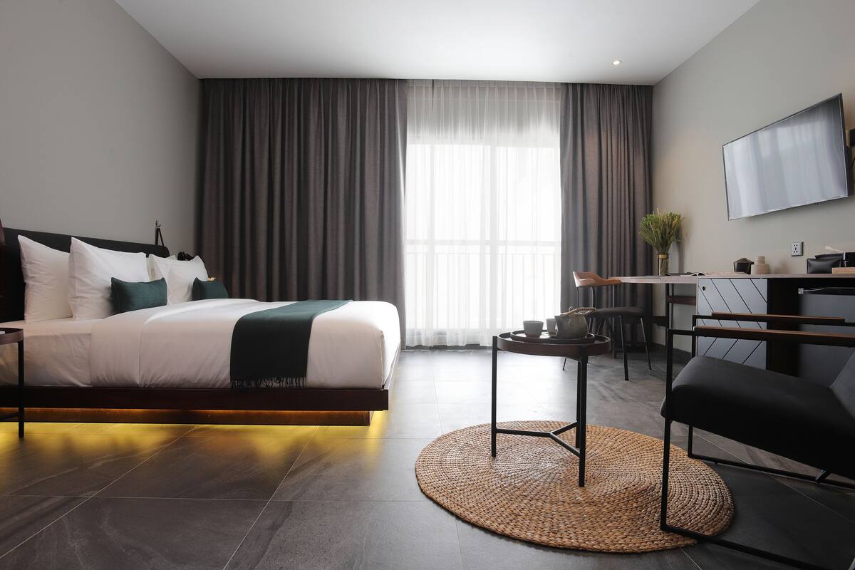 A modern hotel room with a bed, a desk, a chair, and a TV.