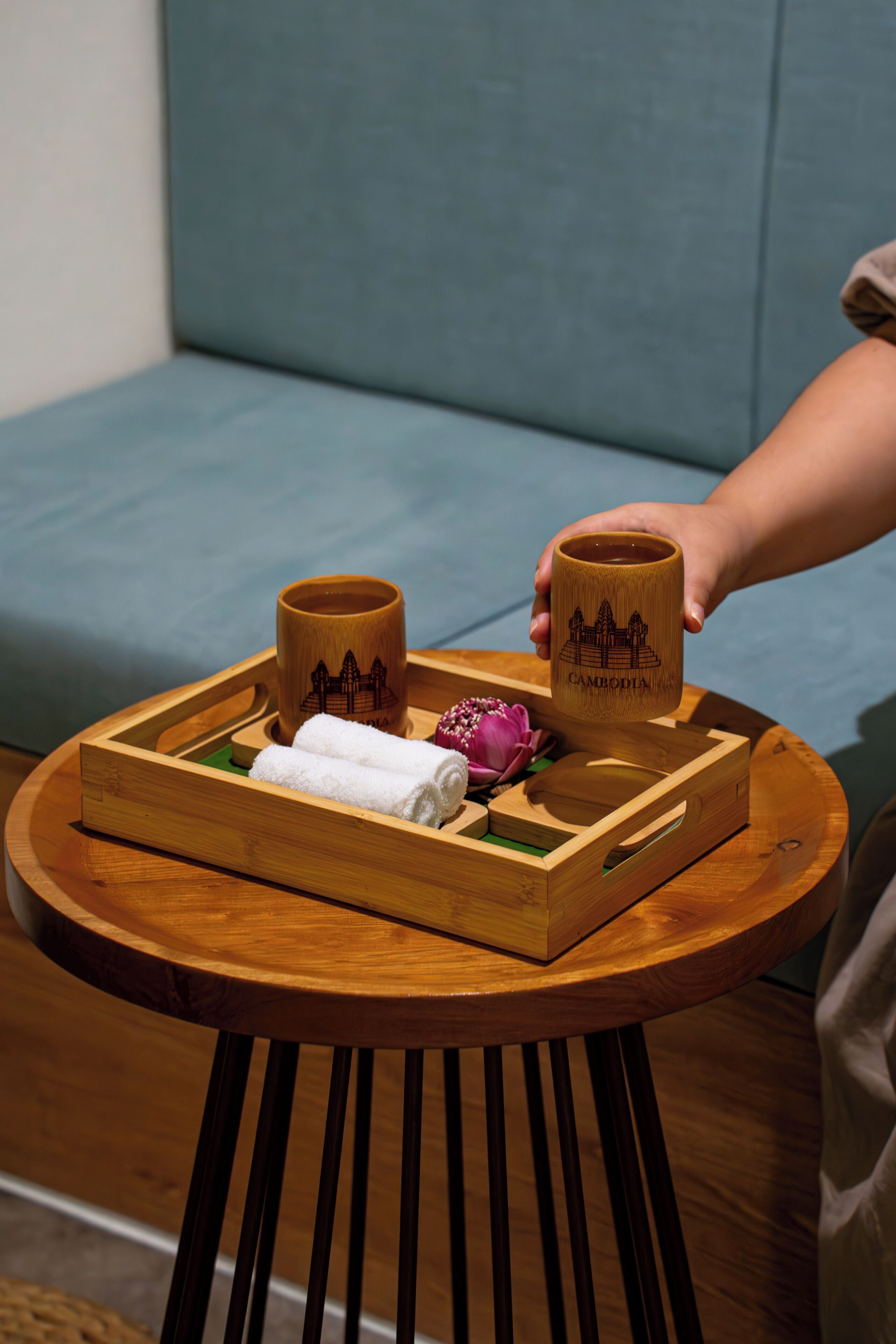 A wooden tray with two mugs and a towel on a round wooden table.