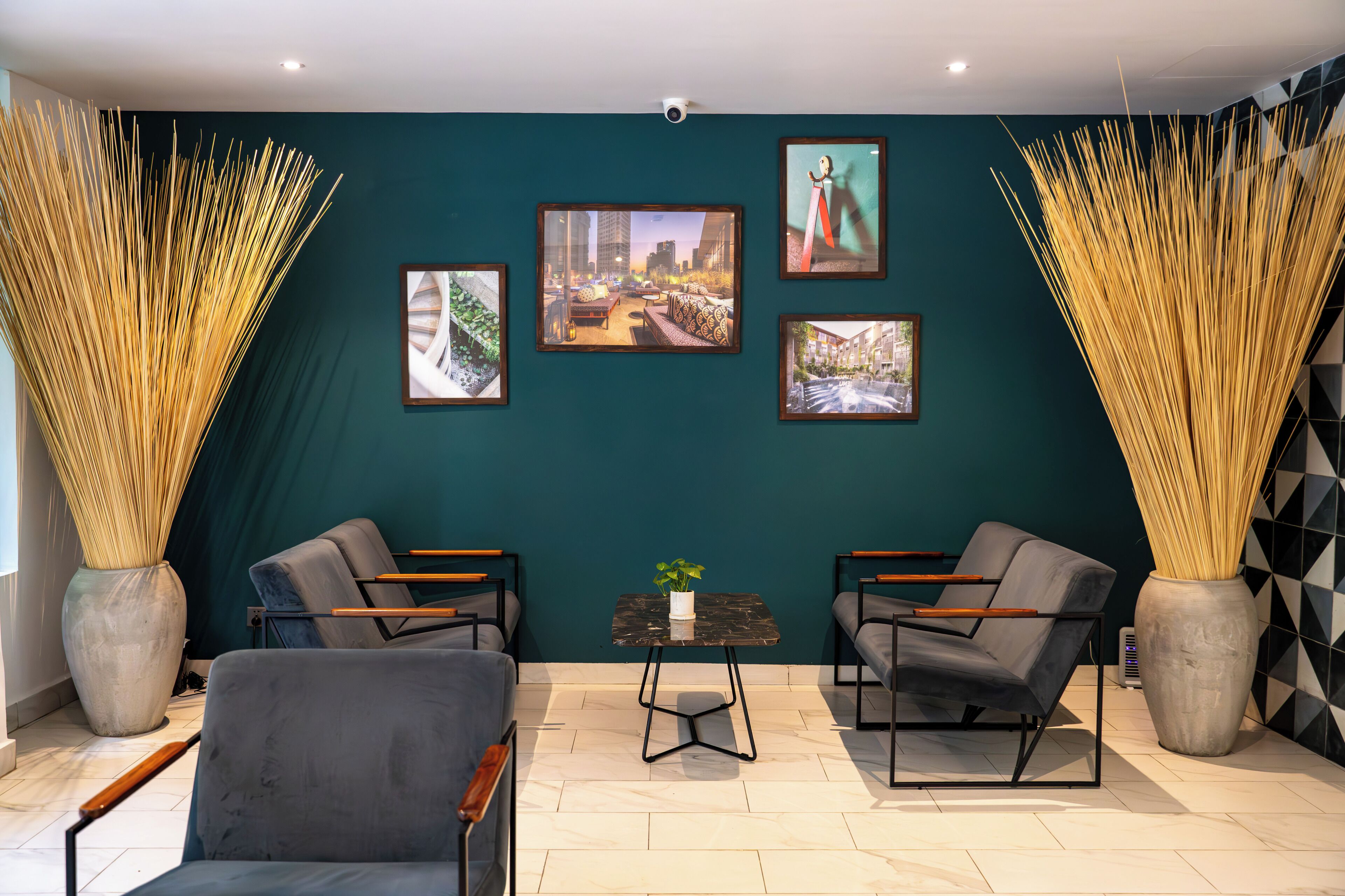 A modern interior with teal walls, framed artwork, two sofas, a small table, and tall decorative vases.