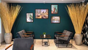 A modern interior with teal walls, framed artwork, two sofas, a small table, and tall decorative vases.
