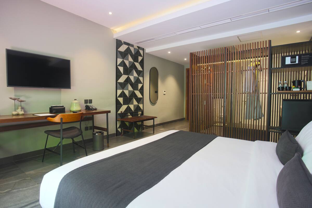 A hotel room with a large bed, a desk with a chair, a television, and a decorative wall panel.