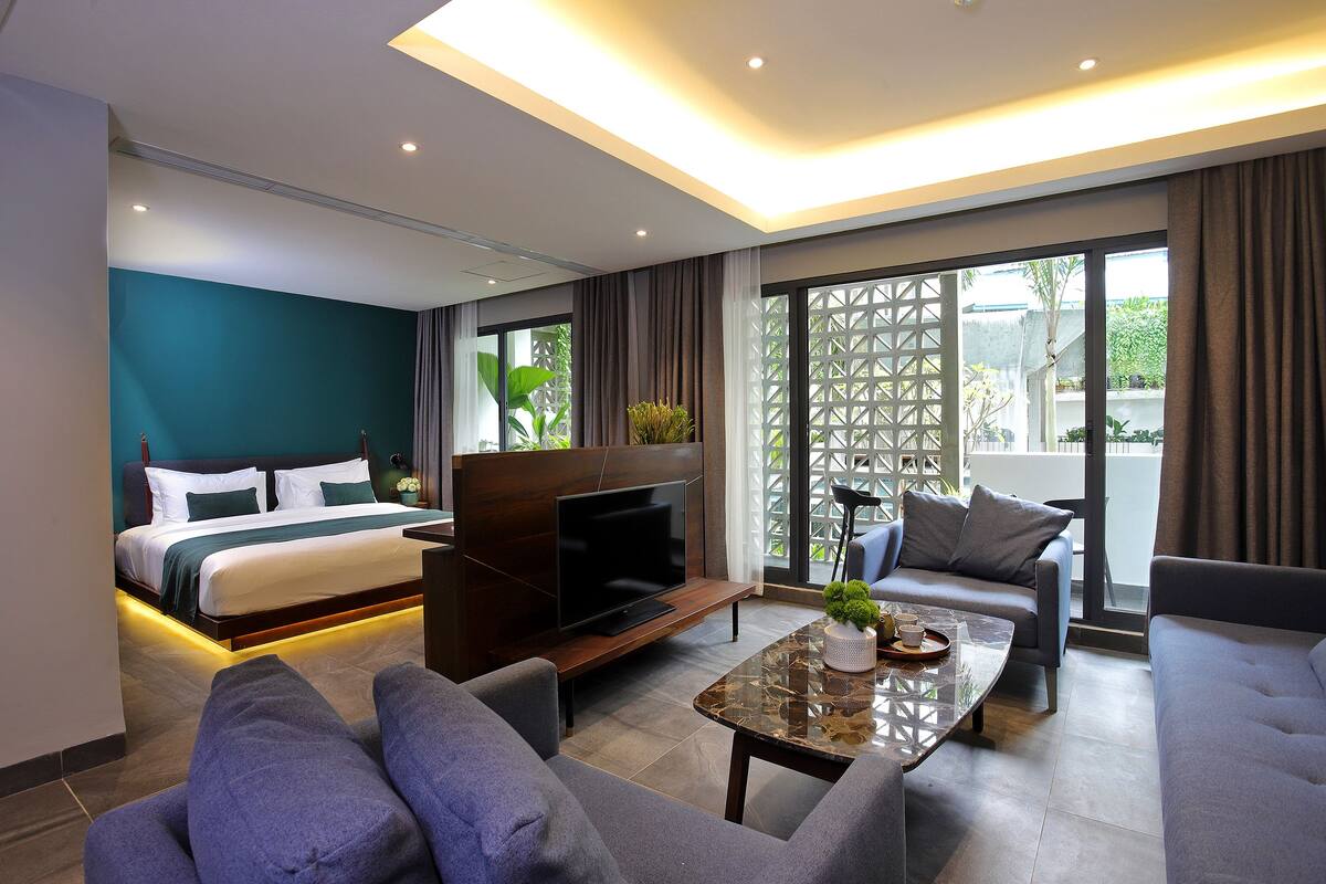 A modern hotel room with a bed, sofa, TV, and a balcony with a view.