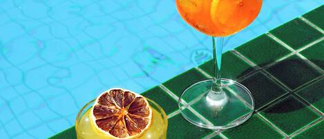 Two glasses of beverages on a tiled surface by a pool.