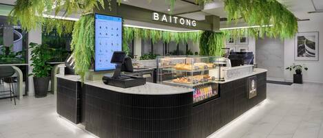 A modern reception area with a curved counter, a digital menu board, and a display case with pastries.