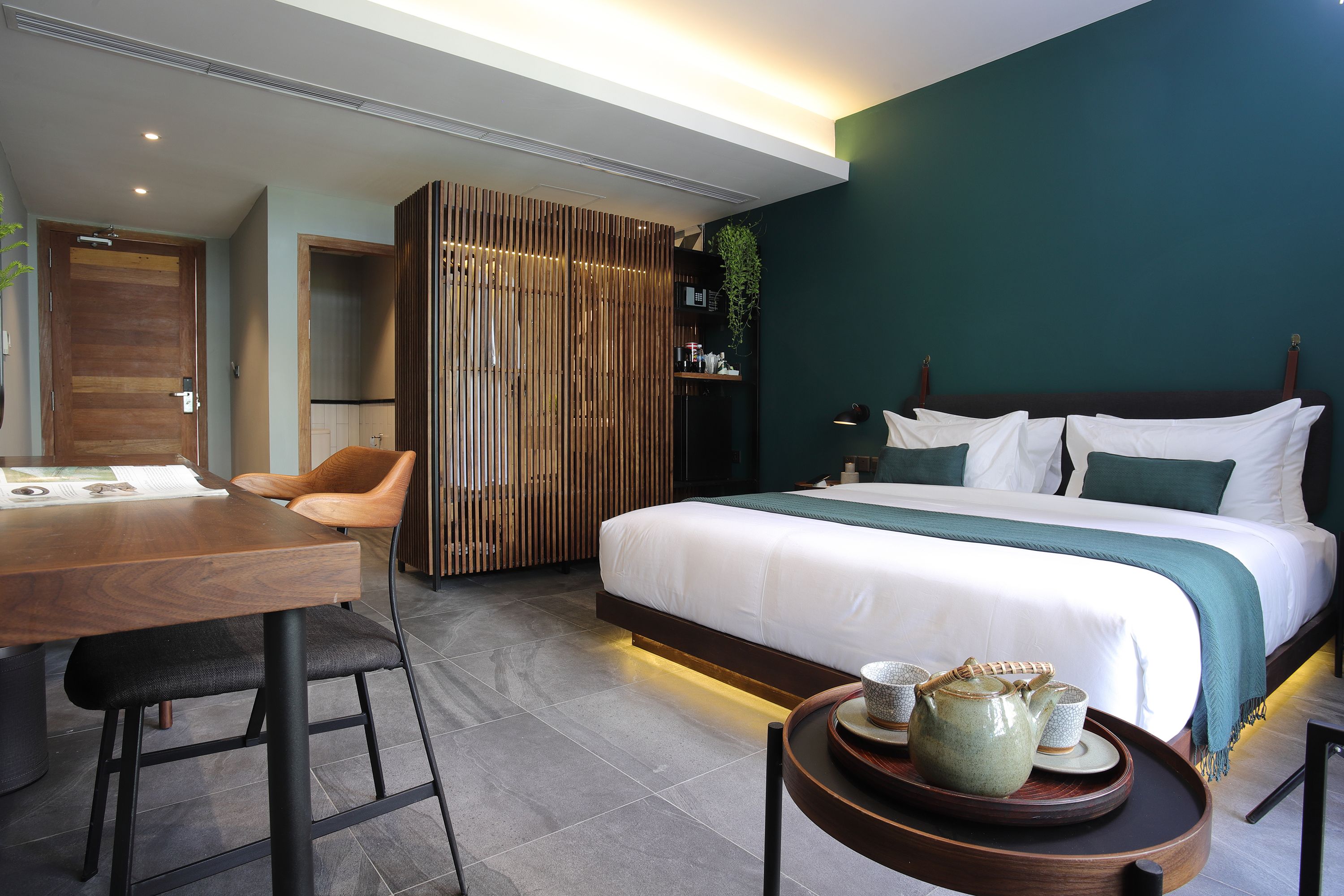 A modern hotel room with a large bed, a wooden desk, and a dining table.