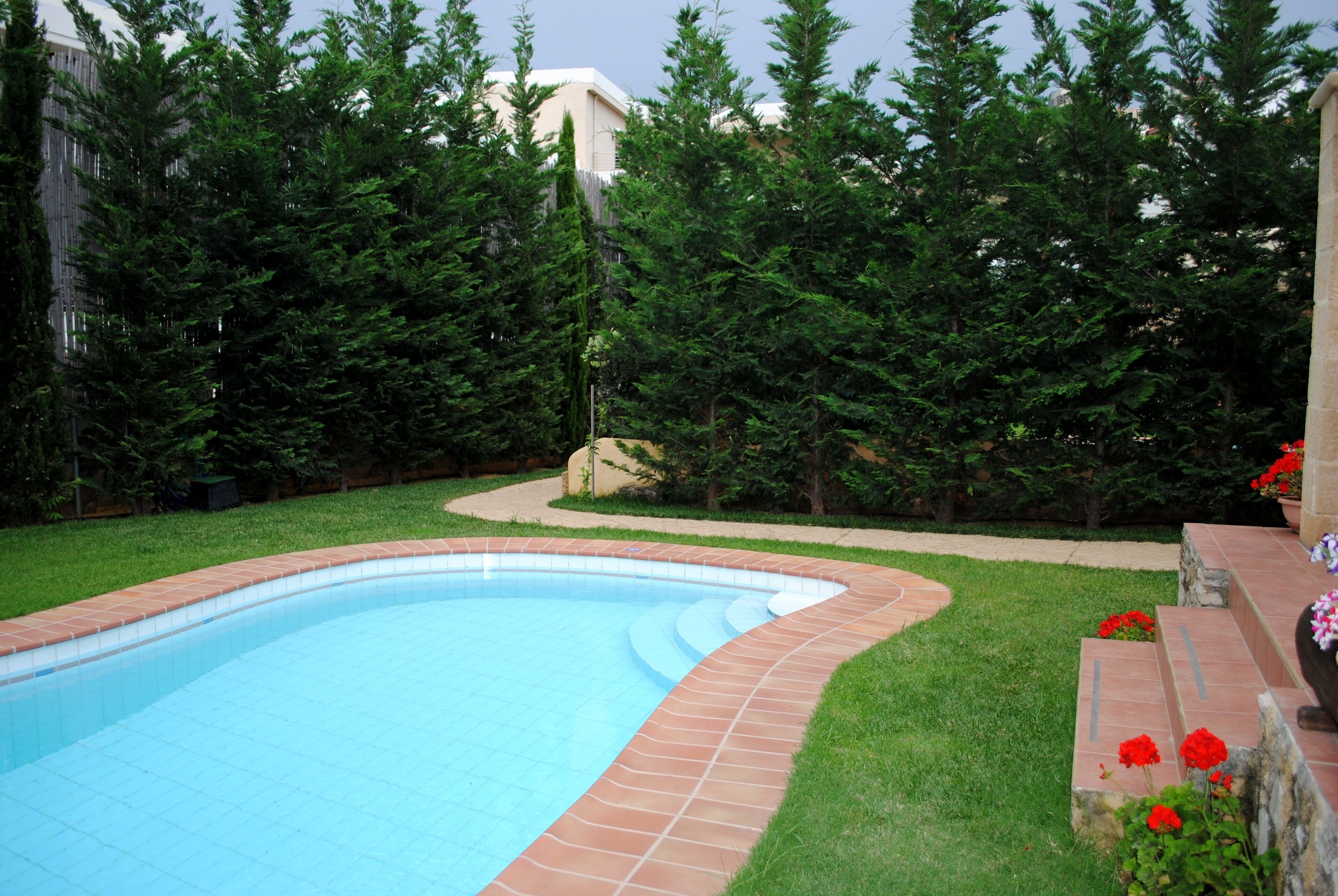 A swimming pool with a tiled edge, surrounded by a grassy area and trees.