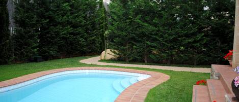 A swimming pool with a tiled edge, surrounded by a grassy area and trees.