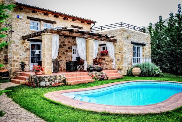 A stone house with a pool, outdoor seating, and a garden.