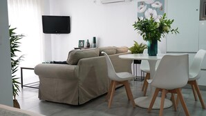 Ett modernt vardagsrum med en beige soffa, vita stolar, ett litet runt bord och en tv som är monterad på väggen.