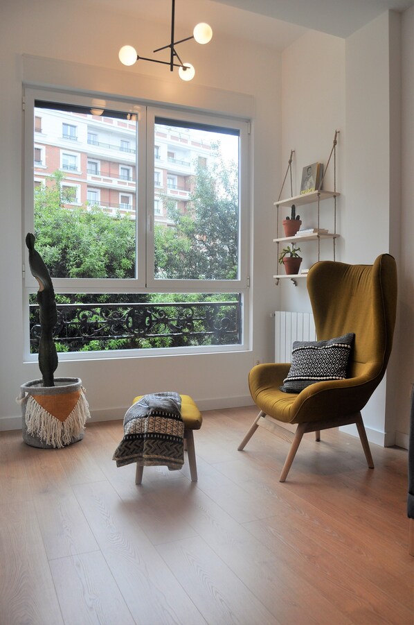 A room with a large window, a chair, a small stool, and a hanging plant. - Donostia Chic Apartment ESS02298 (Donostia)