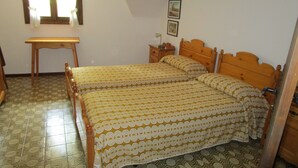 Een slaapkamer met twee houten bedden, een nachtkastje van hout, een klein tafeltje en een raam met gordijnen.