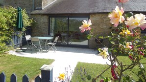 A stone house with a patio, outdoor seating, and a garden with flowers. - Gîtes in peaceful setting, heated pool, river, near Pont Aven Concarneau beaches (Bretagne)