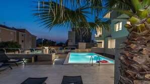 Un espace piscine aménagé sur le toit, avec des chaises longues, une piscine et des palmiers.