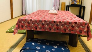 A traditional Japanese room with tatami flooring, a low table with a red patterned tablecloth, a cushion, and a framed picture on a small stand. - Osaka Vacation Home (Osaka)