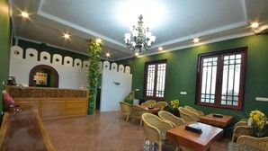 A hotel lobby with a reception desk, wicker furniture, a chandelier, and green walls. - MiCO Hill Resort (Pyin Oo Lwin)