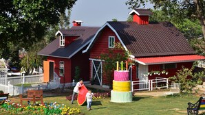 A red house with a metal roof, a white picket fence, and a garden with colorful flowers. - MiCO Hill Resort (Pyin Oo Lwin)
