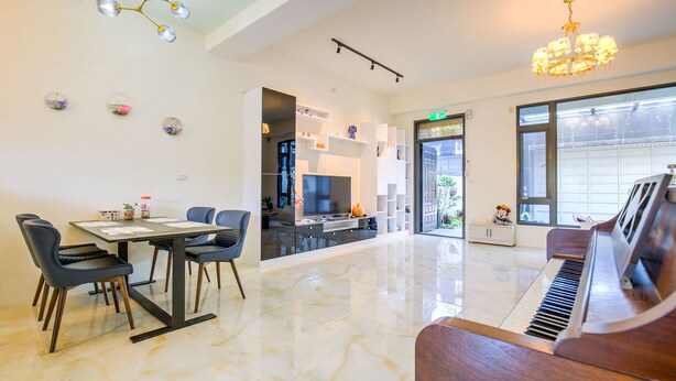 Amplia sala de estar con un piano, una mesa de comedor con sillas, un televisor y una cocina visible a través de una puerta abierta.