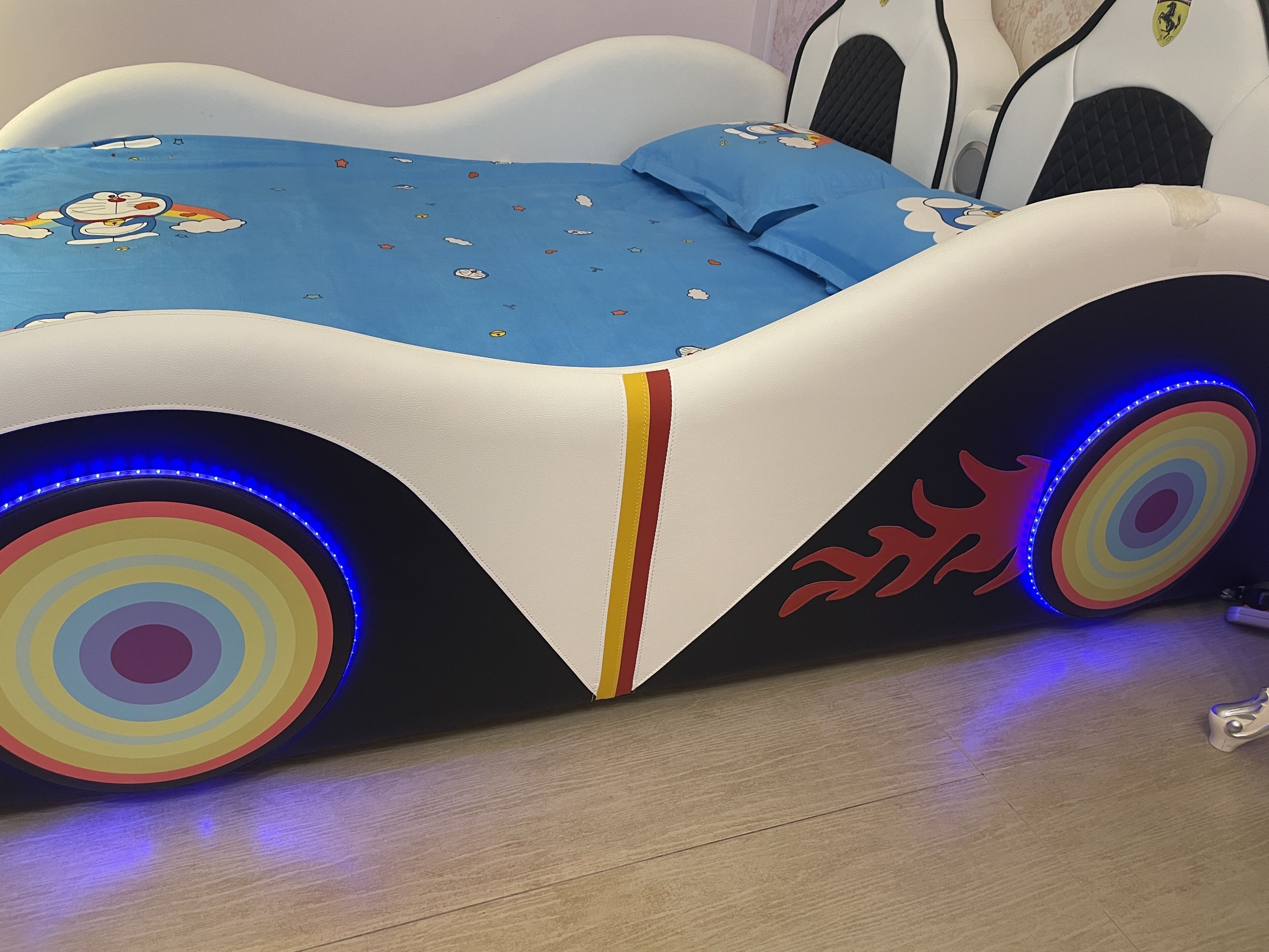 Un lit au design unique, doté d’une tête de lit sur le thème de l’automobile, avec des lumières LED et un motif circulaire coloré sur le côté.