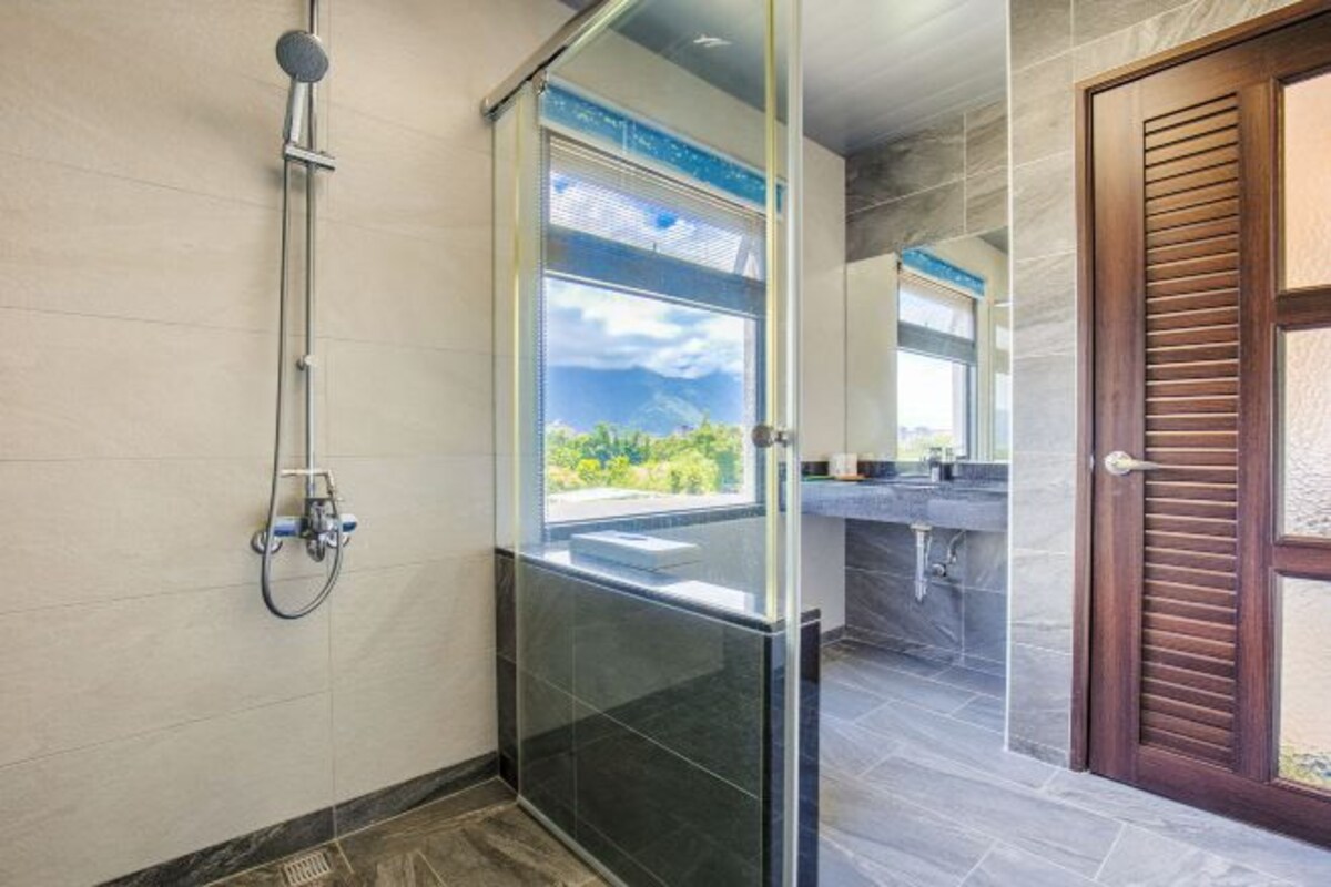 Un baño moderno con cabina de ducha de vidrio, un ventanal grande y vistas a zonas verdes.