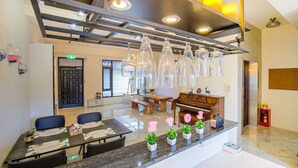 Un área de recepción moderna con mostrador de mármol, asientos, un piano y lámparas decorativas de vidrio.