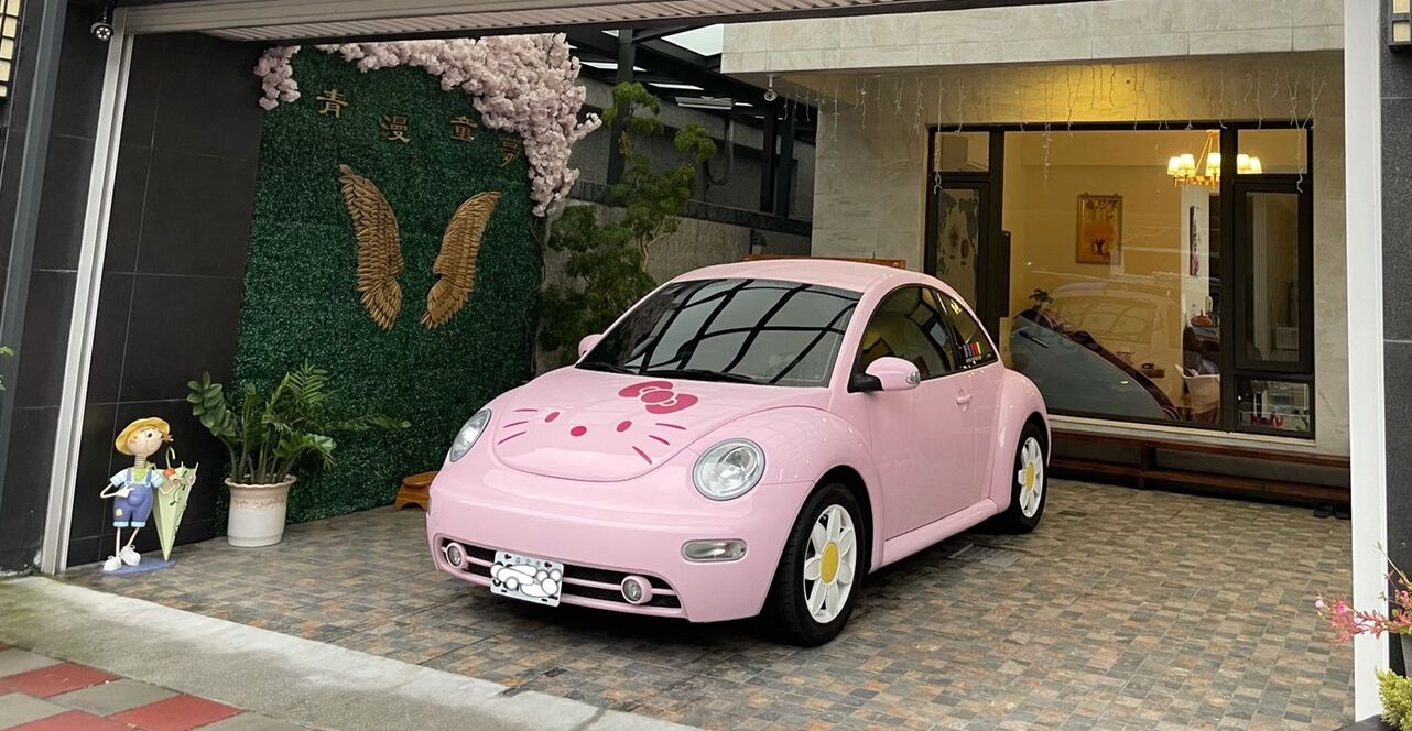 A pink car parked in front of a building with a green wall and a large window.