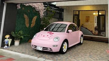 A pink car parked in front of a building with a green wall and a large window.