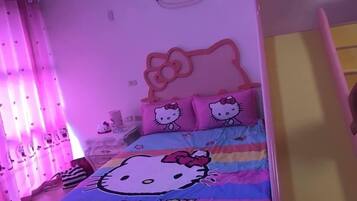 A room with a bed featuring Hello Kitty bedding, pink curtains with Hello Kitty prints, and a Hello Kitty crown on the wall.