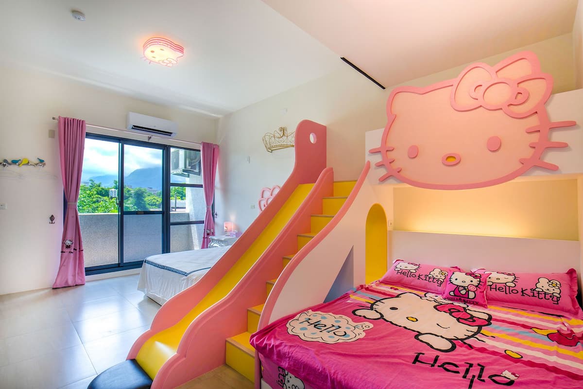Ein Zimmer mit einem Hello Kitty-Themenbett, einer rosa und gelben Rutsche und einem Balkon mit Blick.